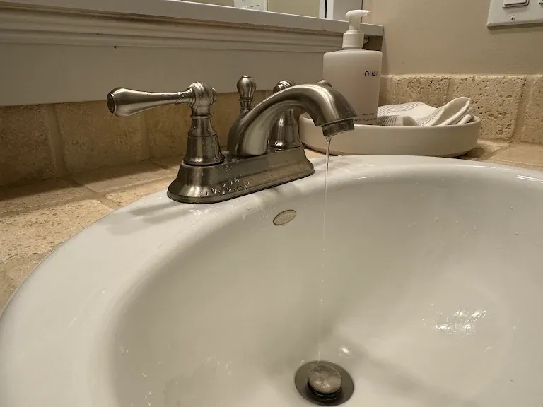 Brushed nickel bathroom faucet dripping into a white sink