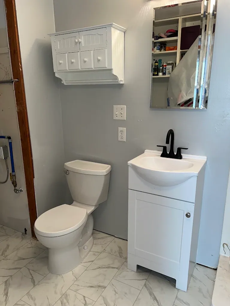 Small bathroom with new toilet, white vanity, black faucet and marble-look tile floor