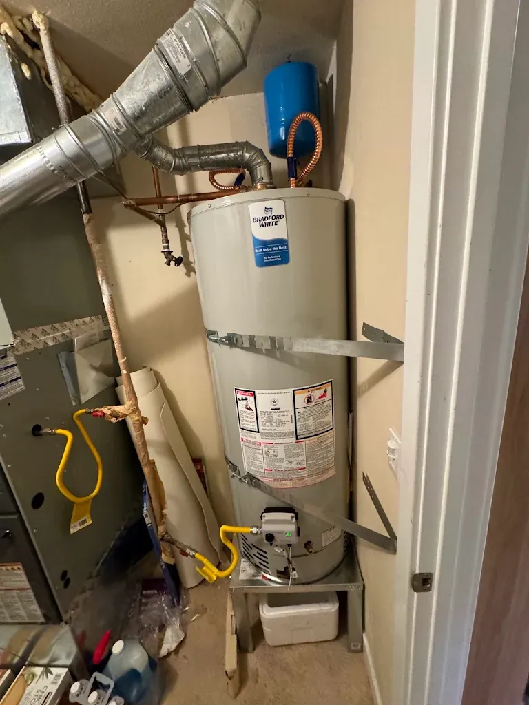 Bradford White gas water heater on a stand in a utility closet next to a furnace