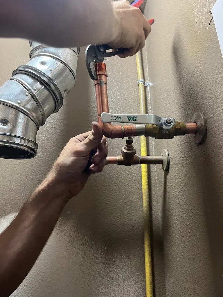 Plumber's hands soldering copper near a new gas ball valve and water heater vent — Gas Line Installation & Repair for Ruston homes