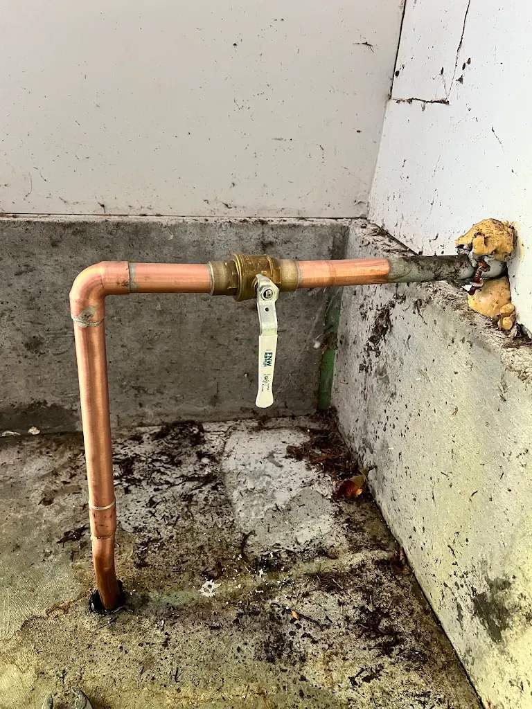 Copper water main entry with ball valve along an exterior concrete wall