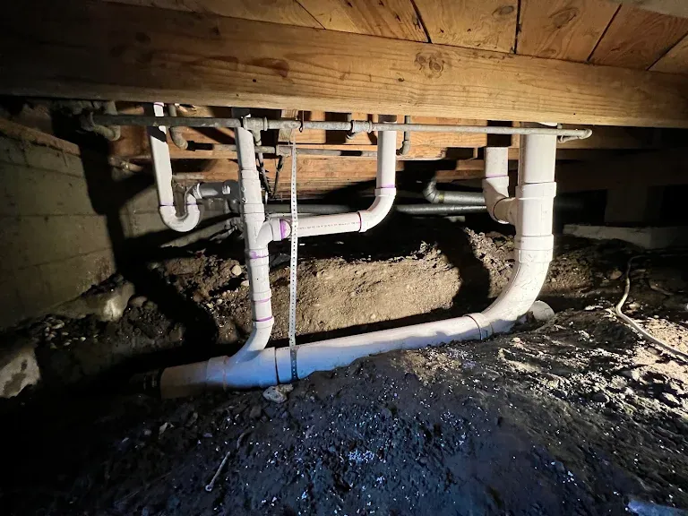 New white PVC drain lines installed under floor joists in a crawlspace