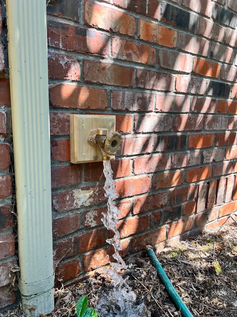 New brass hose bib mounted on a wood block on a brick wall with water running