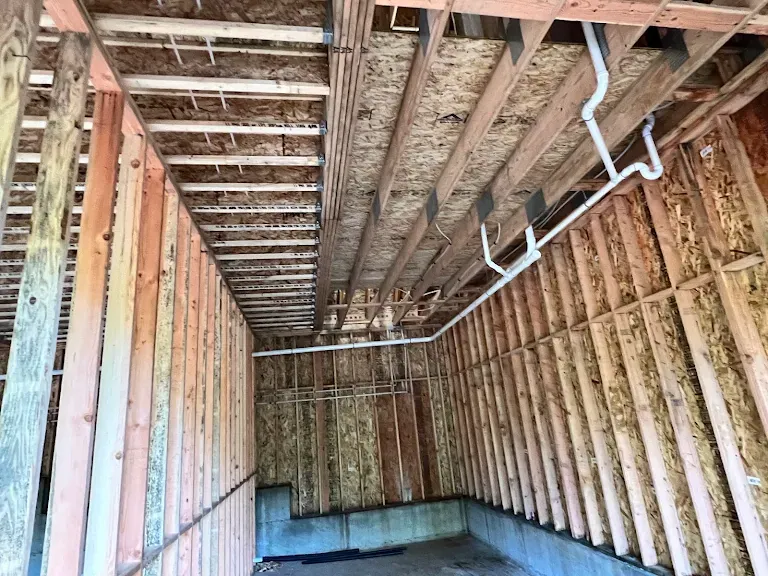 Framed shop interior with white PVC drain-waste-vent piping run along the ceiling joists