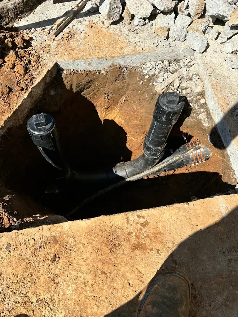 New two-way sewer cleanout risers installed in an excavated area next to broken concrete