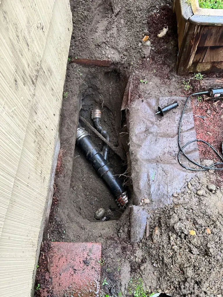 Excavated trench beside a house showing new ABS sewer pipe and fittings