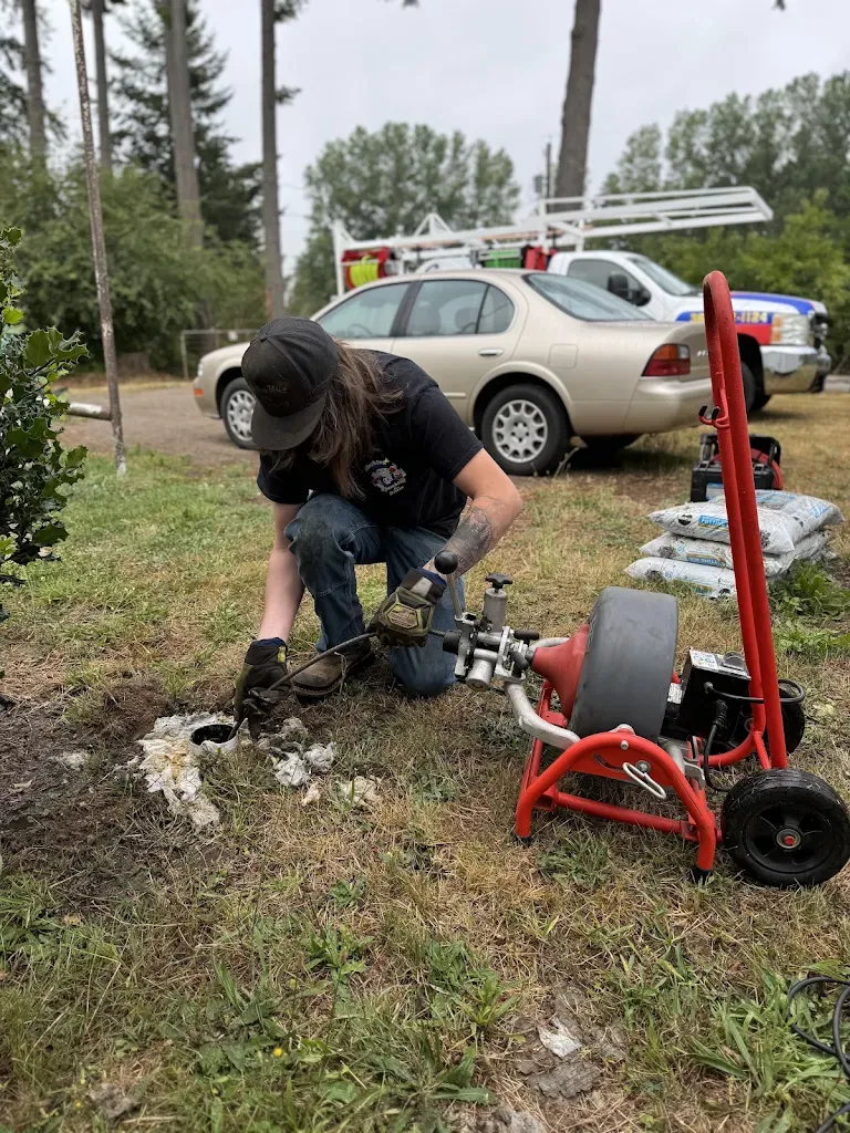 Plumber running a drum drain machine into an exterior sewer cleanout in a front yard