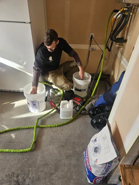 Plumber flushing a tankless water heater with a descaling pump and buckets in a garage