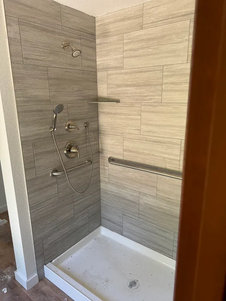 Tile shower with brushed nickel fixtures and grab bars, low-threshold base
