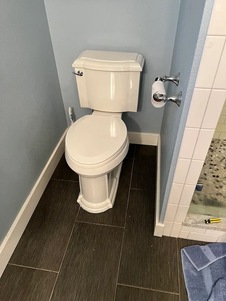 New white two-piece toilet installed in a bathroom with dark tile floor and blue walls