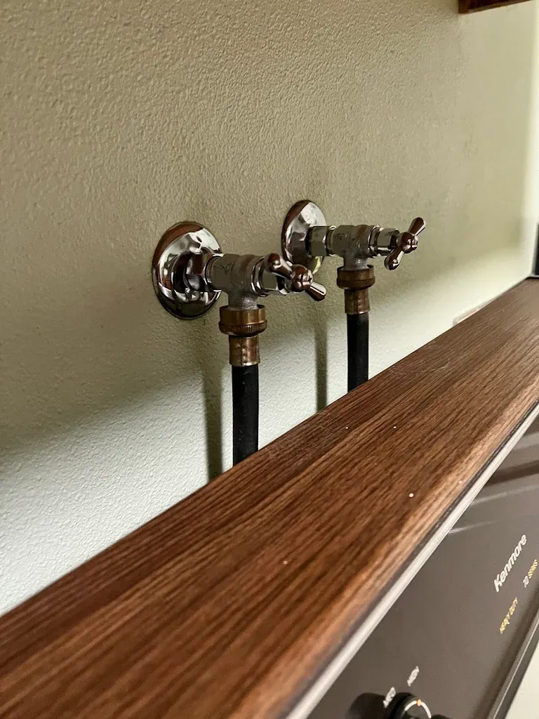 Pair of new chrome washing machine shutoff valves on a laundry room wall