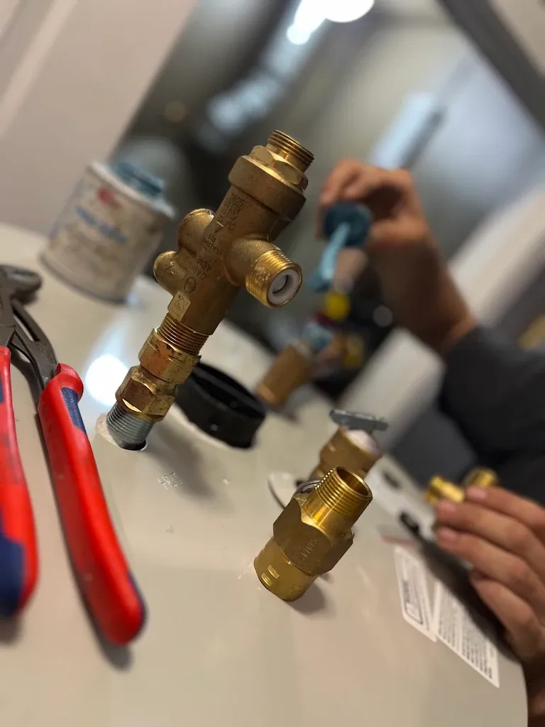 Brass thermostatic mixing valve and T&P relief valve parts laid out on a water heater during installation