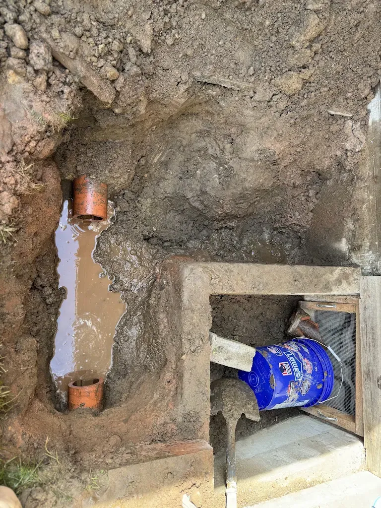 Excavated sewer pipe showing orange pipe and standing water at a foundation — Water Line Repair & Replacement for Grapeview homes